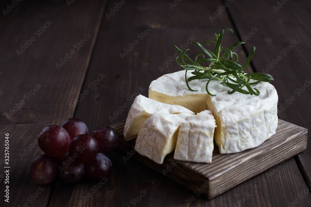 Camembert cheese, red grapes ,fresh rasmarin on a wooden stand on a dark wood background