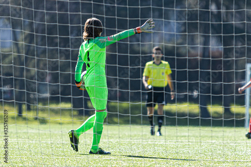 Young soccer goalkeeper behind his goal stopping a goal, back view