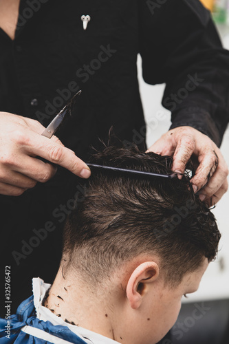 Hairdresser cuts the hair of a boy with scissors