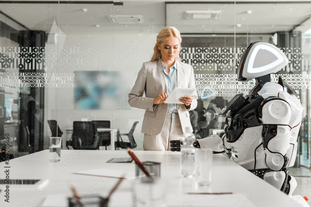 attractive businesswoman using digital tablet while standing near robot in meeting room attractive businesswoman using digital tablet while standing near robot in meeting room