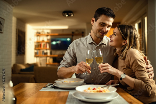 Young loving couple embracing while toasting with Champagne during dinner.