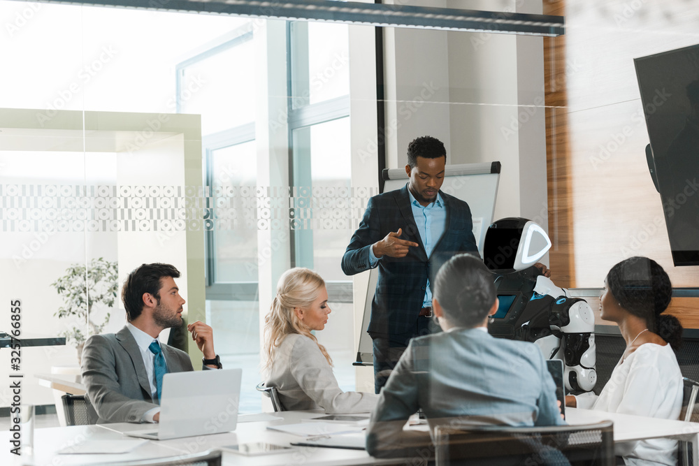 Fototapeta premium handsome african american businessman showing robot to multicultural colleagues in office