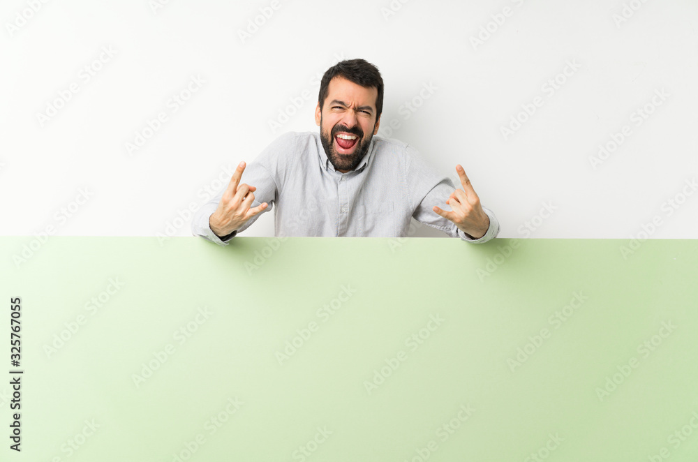 Young handsome man with beard holding a big green empty placard making rock gesture Young handsome man with beard holding a big green empty placard making rock gesture