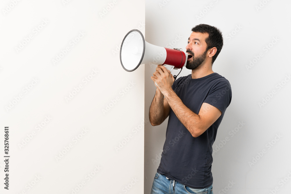 Young handsome man with beard holding a big empty placard shouting through a megaphone Young handsome man with beard holding a big empty placard shouting through a megaphone