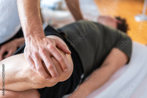 Close-up of a professional masseur therapist giving leg massage to a strong man lying in the spa center. Selective focus on hands