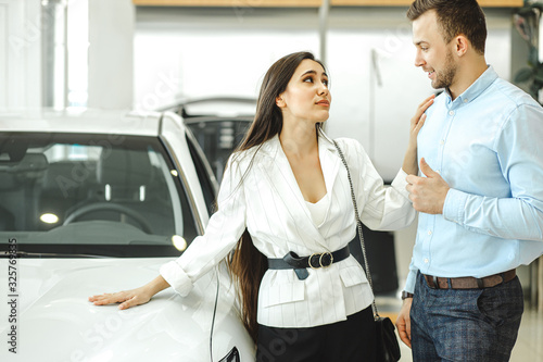 portrait of young beautiful woman begging her husband to buy new auto in dealership. married couple looking for new car