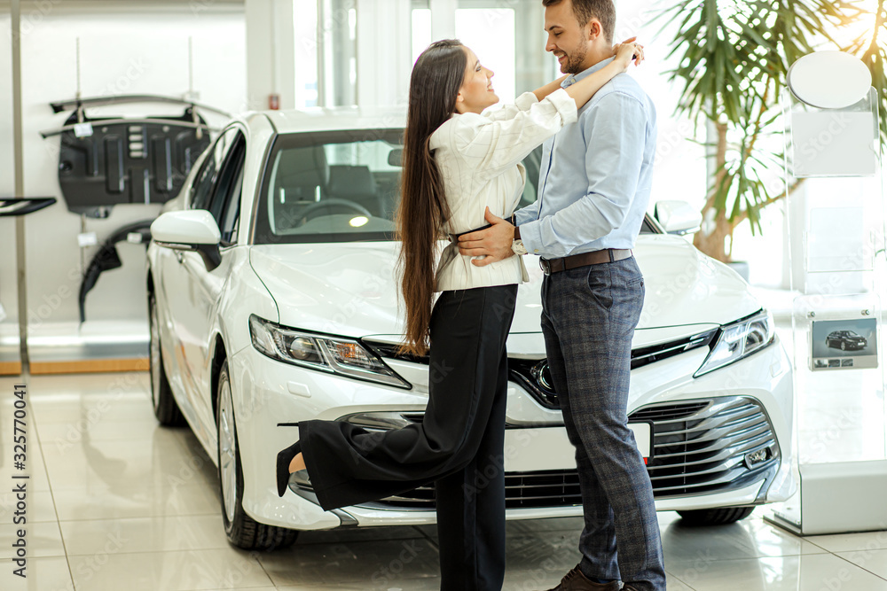 young family bought beautiful new car in dealership, now they are owners of chic automobile. side view on couple hugging. automobile, car, vehicle, dealership concept young family bought beautiful new car in dealership, now they are owners of chic automobile. side view on couple hugging. automobile, car, vehicle, dealership concept