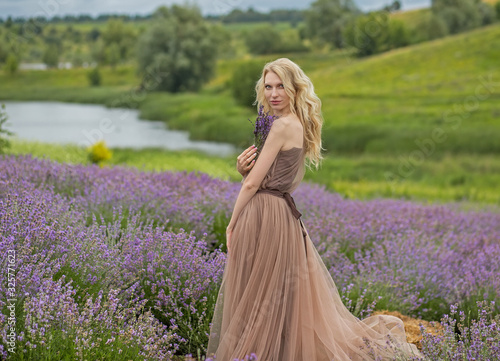  young blonde long-haired girl in a flying brown dress enjoys nature in a lavender field, background against the background of a lake and lavender