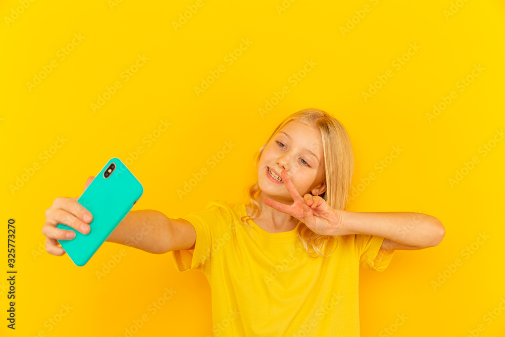 Smiling little girl kid showing blue screen of new popular mobile phone on light yellow background