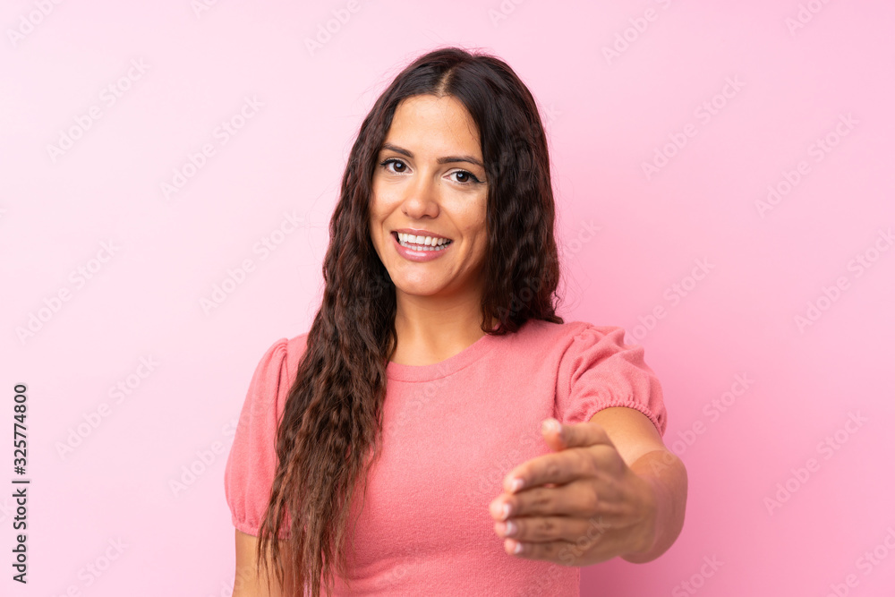 Young woman over isolated pink background handshaking after good deal Young woman over isolated pink background handshaking after good deal