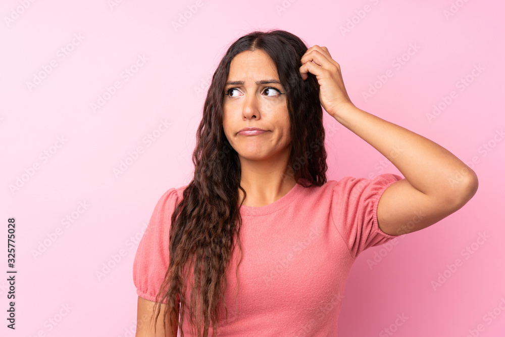 Young woman over isolated pink background having doubts and with confuse face expression