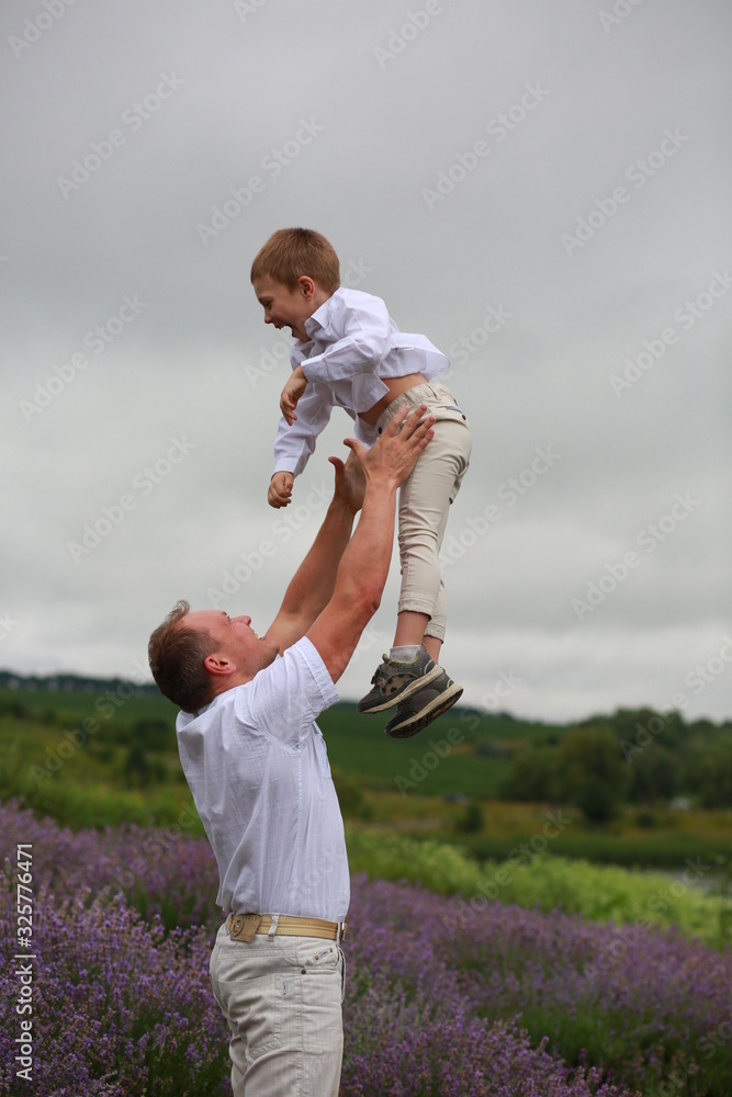 Fototapeta premium happy father rises to the sky little son up, having fun and relaxing in a lavender field in summer