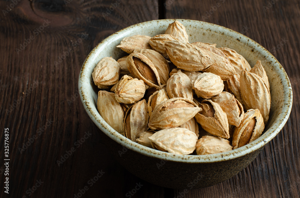 Almonds in nutshell in cup on wooden background Almonds in nutshell in cup on wooden background