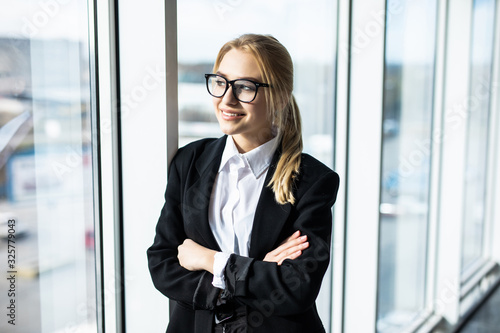 Attractive businesswoman standing in front of windows in an office building overlooking the city