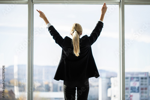 Confident businesswoman spreading hands standing at office window, enjoying big city, successful entrepreneur celebrating business success with arms open wide, feeling powerful inspired, rear view