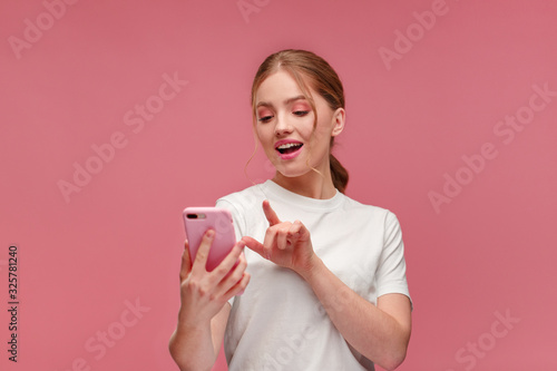 Funny young redhead woman holding pink smartphone and smiling.Happy girl using mobile phone apps, texting message, browsing internet, looking at smartphone. Young people working with mobile devices