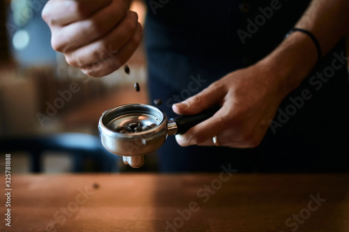 man throwing coffee beans into the portafilter, close up side view photo