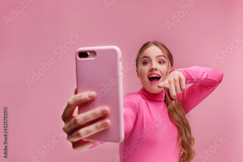 The best day ever. Surpised young redhead woman holding pink smartphone, smiling and expressing positivity. Happy girl got shocking positive news. Copy space. Young people working with mobile devices. photo