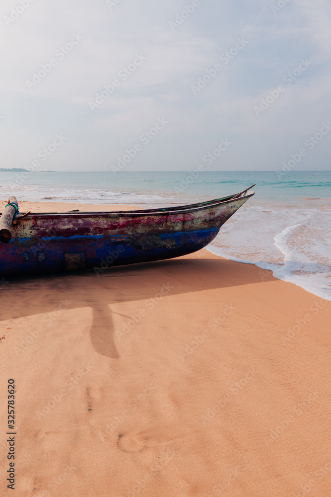 Traditional fisherman's boat on the sand of Sri Lanka island beach on a ocean coast in front of turquoise ocean waves.