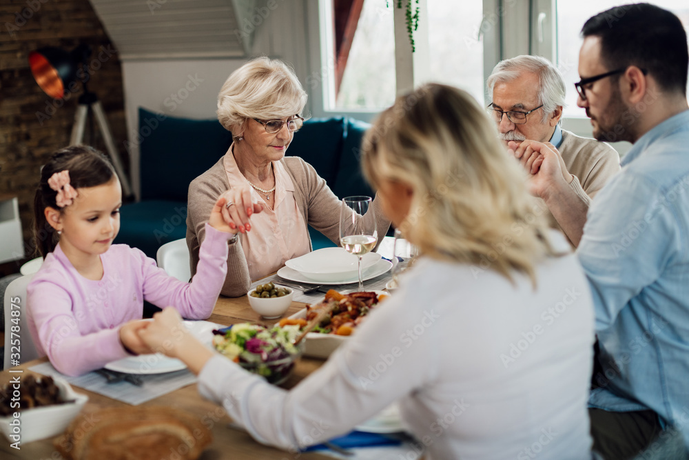 Multi-generating family saying grace while holding hands at dining table. Multi-generating family saying grace while holding hands at dining table.