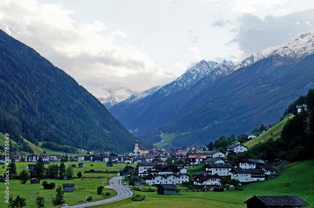 Blick auf Neustift im Stubaital in Tirol, markante Kirche umgeben von Häusern und hohen Bergen, im Hintergrund der Stubaier Gletscher