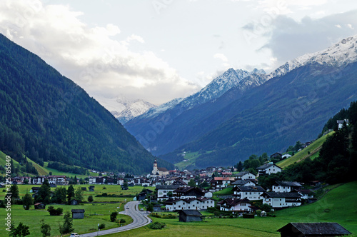 Blick auf Neustift im Stubaital in Tirol, markante Kirche umgeben von Häusern und hohen Bergen, im Hintergrund der Stubaier Gletscher