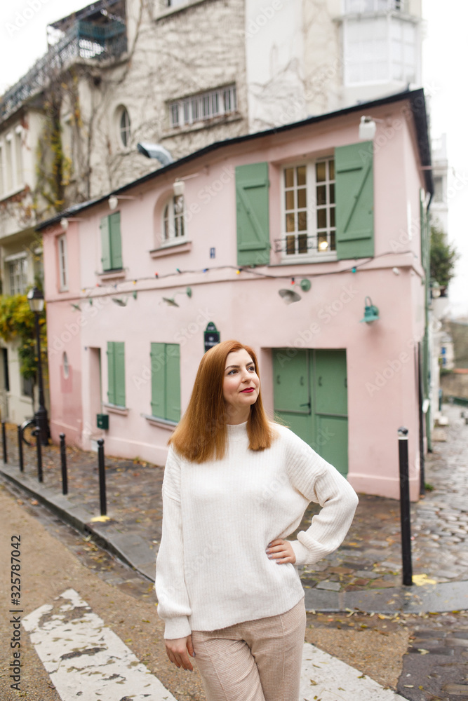 Young beautiful girl dressed in a white sweater and pink pants, walks along the beautiful streets of Paris against the backdrop of a pink house