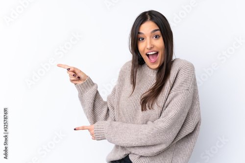 Young brunette woman over isolated white background surprised and pointing side