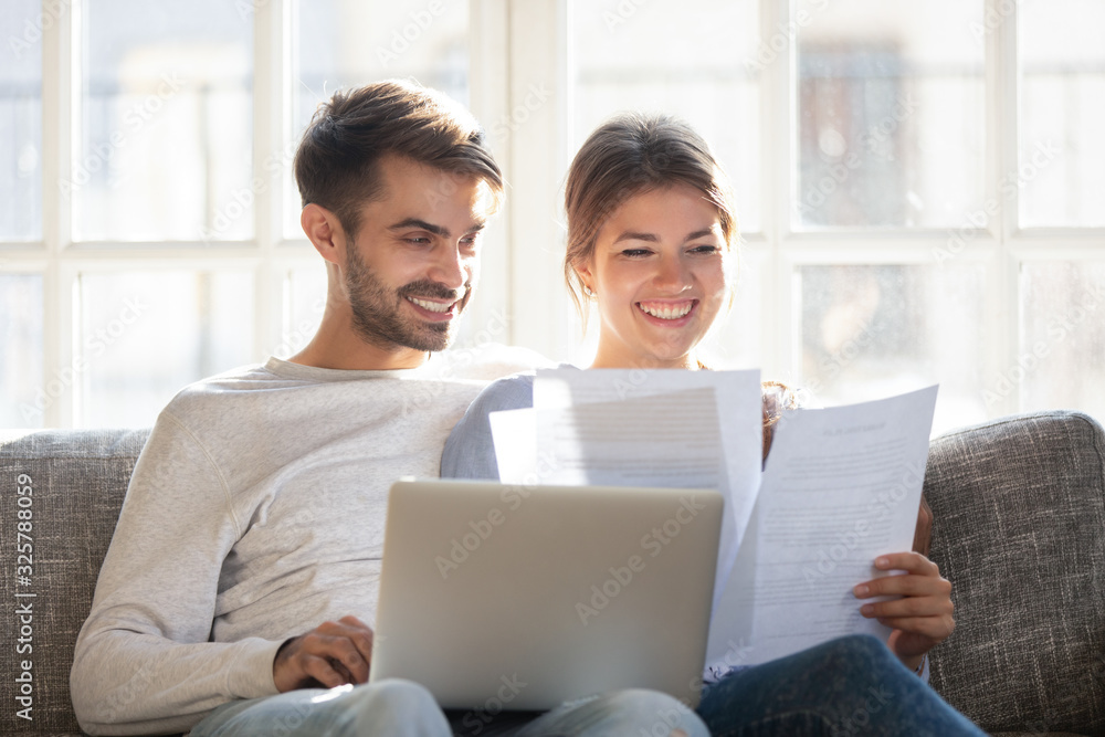 Smiling couple hold paperwork paying bills online Smiling couple hold paperwork paying bills online