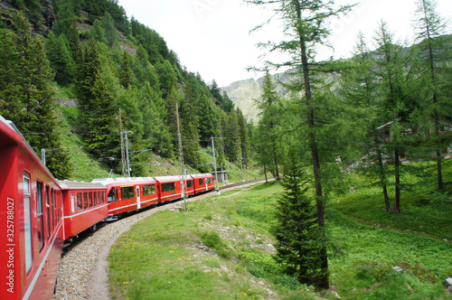 Ein Zug der Rhätischen Bahn mit roten Wagen, Fahrt durch eine Landschaft in Graubünden, Schweiz