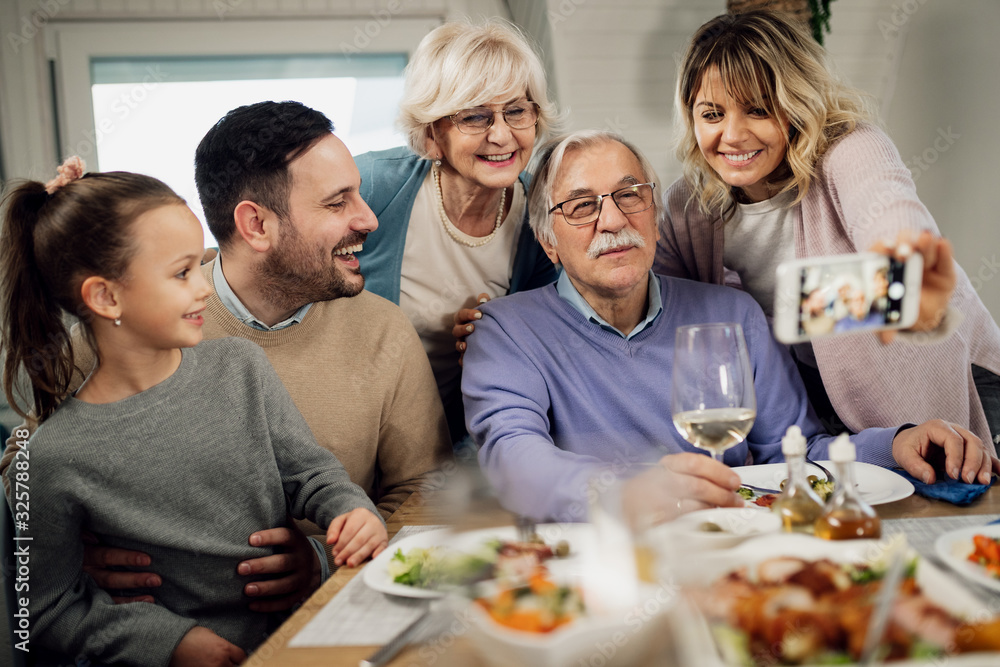 Happy extended family using smart phone and taking selfie in dining room. Happy extended family using smart phone and taking selfie in dining room.