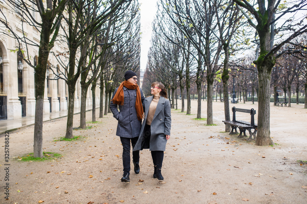 Young beautiful couple dressed stylishly, a girl in a gray coat, a man in a gray coat are walking in a park in Paris France