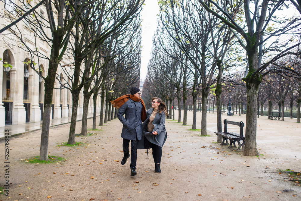 Young beautiful couple dressed stylishly, a girl in a gray coat, a man in a gray coat are walking in a park in Paris France Young beautiful couple dressed stylishly, a girl in a gray coat, a man in a gray coat are walking in a park in Paris France