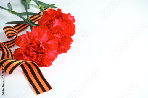 Three red carnations and St. George ribbon (Russian symbol) on a white uniform background. Greeting card for the holiday of the great victory of May 9. photo