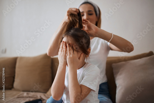 girl doesn't want to have her hair brushed. close up photo. kid feels bad, because mother pulls her hair, kid covering her face with palms, hands