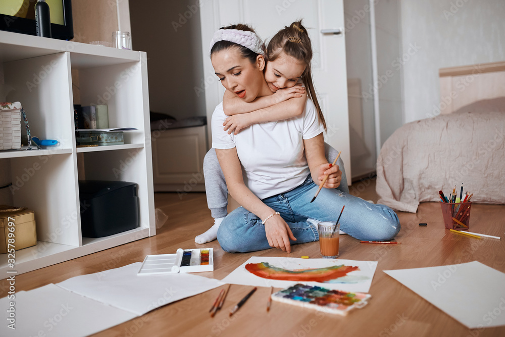 young slim good looking woman holding a brush, her daughter standing behind her and hugging, friendship, love, family young slim good looking woman holding a brush, her daughter standing behind her and hugging, friendship, love, family