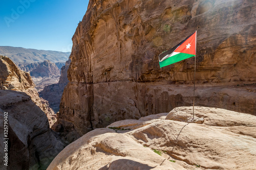 Cliffs and Jordanian flag under the sunlight. I enjoyed the amazing views from the scenery Monastery Route, beautiful sunny day at Petra complex and tourist attraction, Hashemite Kingdom of Jordan photo