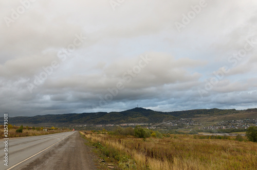 Heavy grey clouds in the cold autumn sky over village with small houses far away in the mountains and fields. Travelling. People living. Roads 