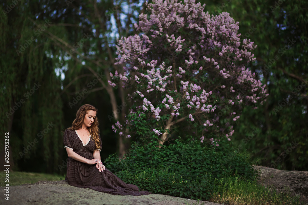Beautiful redhead young woman posing in a long dress by a blooming lilac in the spring Beautiful redhead young woman posing in a long dress by a blooming lilac in the spring