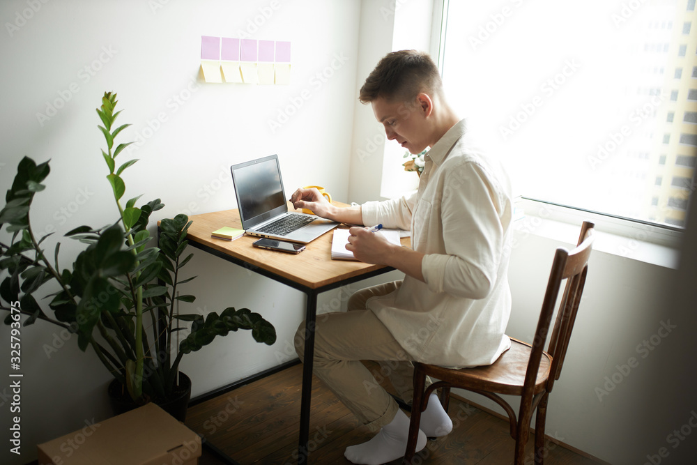young journalist writing a report at home. close up side view photo. pleasant male designer writing on the notepad, notebook young journalist writing a report at home. close up side view photo. pleasant male designer writing on the notepad, notebook