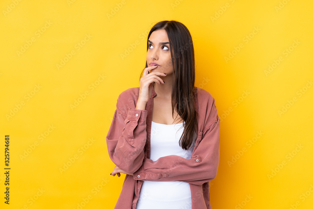 Young brunette woman over isolated yellow background having doubts and with confuse face expression Young brunette woman over isolated yellow background having doubts and with confuse face expression