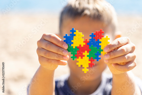 Schilderij op canvas Boy holding colorful puzzle heart in front of his face