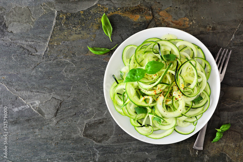 Healthy zucchini pasta topped with garlic and basil. Top view on a dark slate stone background.