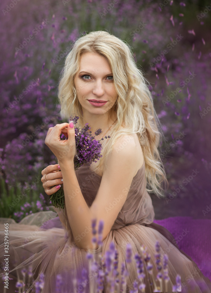 Naklejka premium beautiful blonde girl in a light flying dress in a lavender field in summer enjoying her holidays