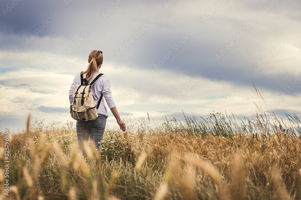 Woman with backpack hiking in field at summer