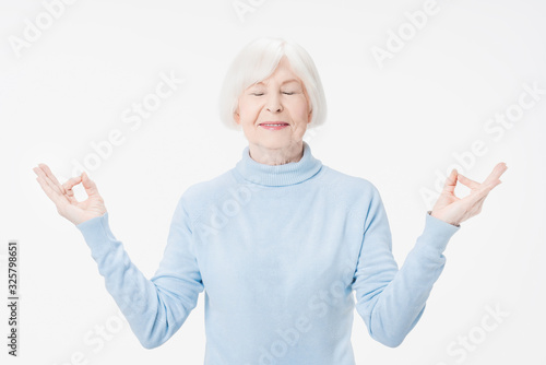 Senior woman relax with eyes closed doing meditation gesture with fingers standing over isolated white background