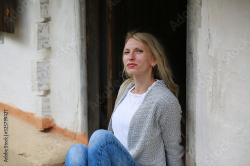  Blond girl with mini jeans resting on the porch of an old Ukrainian-style house