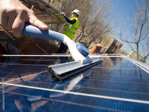Hand cleaning solar panels with a glass cleaner wiper and caucasian seasoned technician cleaning the solar panels with a mop