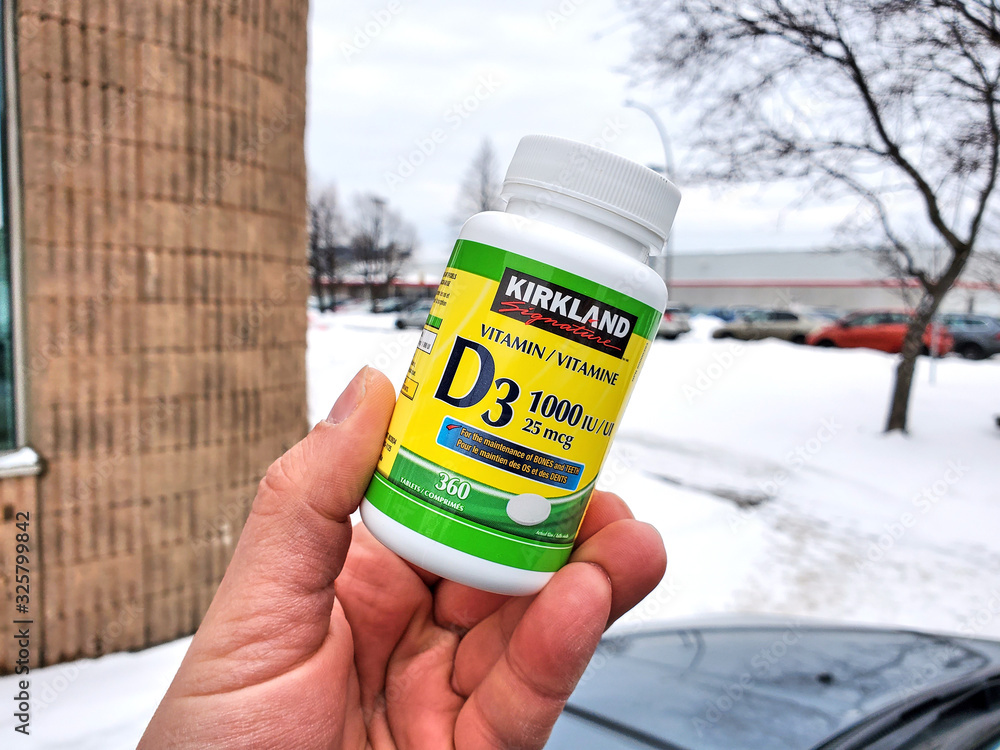 A hand holding Vitamin D pack over Costco warehouse background. Stock