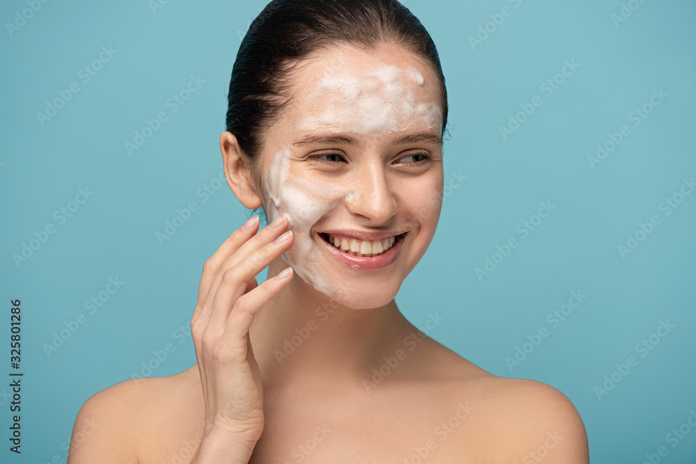 beautiful happy young woman applying cleansing foam on face, isolated on blue beautiful happy young woman applying cleansing foam on face, isolated on blue
